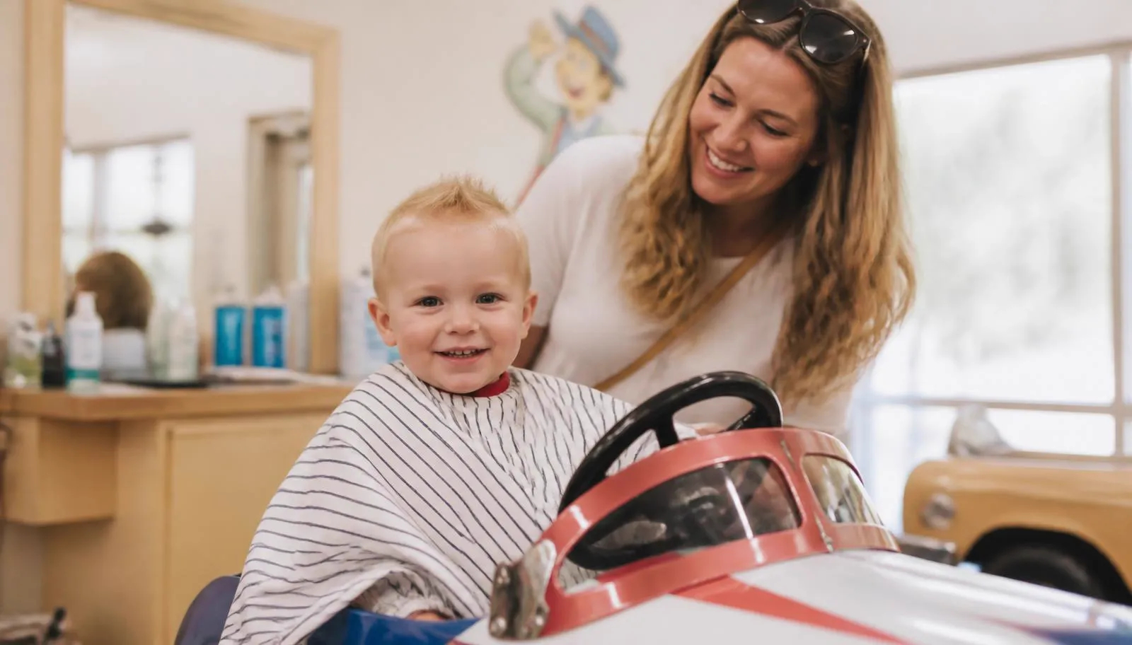 A smiling toddler in a car shaped styling chair at Kidstyles Salon in Bedford Hills